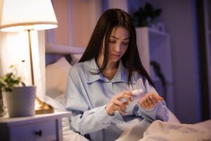 Woman sitting on her bed, taking a pill