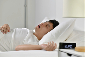 Young man snoring in bed with digital alarm clock on bedside table