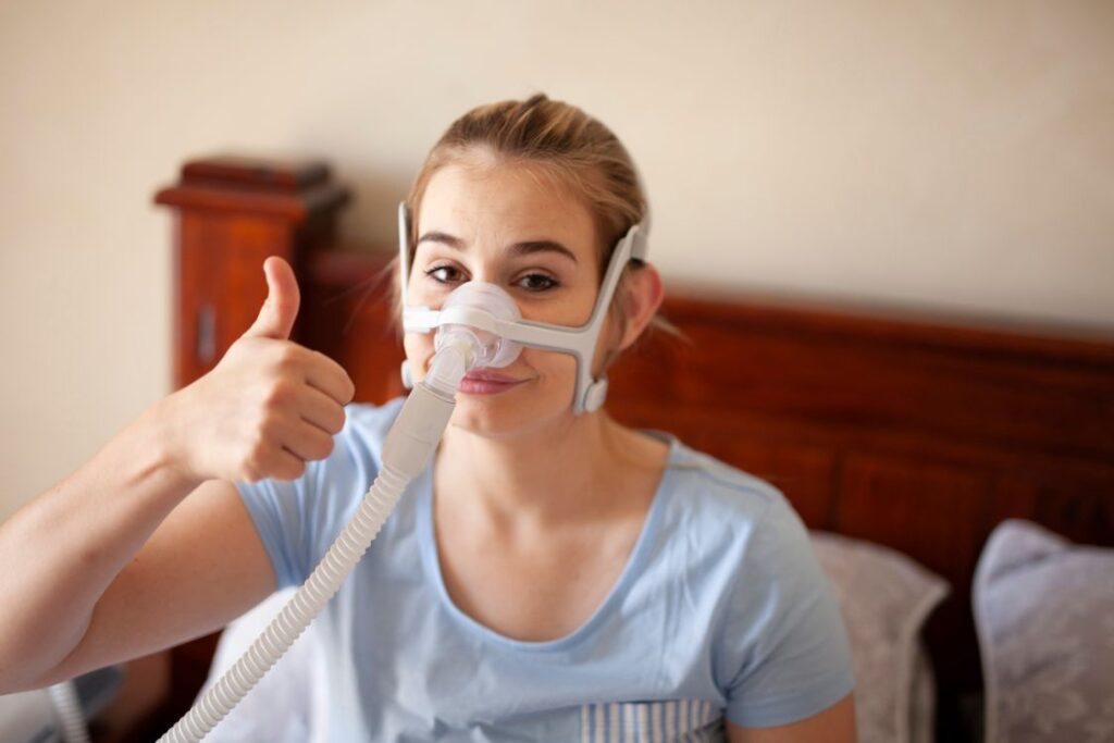 A woman giving a thumbs up while using a CPAP machine